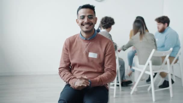 Porträt eines fröhlichen, lächelnd in die Kamera blickenden Mannes, der bei einem Treffen der Selbsthilfegruppe vor Freude sitzt — Stockvideo