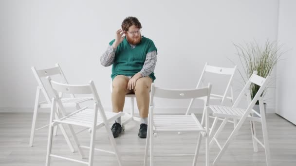 Cara inseguro sentado na sala branca sozinho à espera de terapia de grupo sentindo-se nervoso — Vídeo de Stock