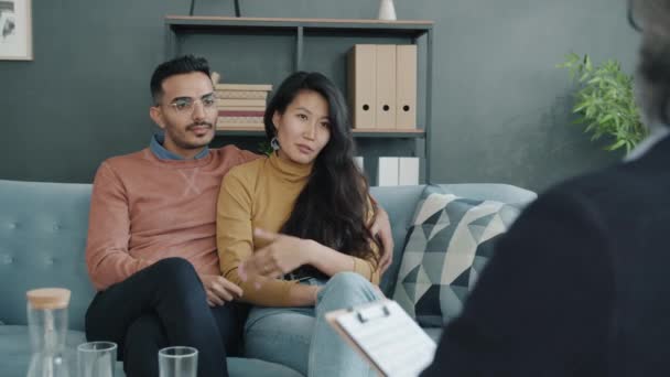 Pareja birracial compartiendo problemas maritales con el terapeuta durante la consulta familiar en el consultorio — Vídeos de Stock