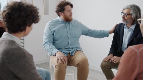Buclatý chlap diskutovat problémy s lidmi během skupinové terapie v bílé barvě studia — Stock video