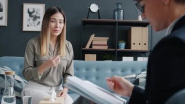 Stresli kadın psikoterapistle sorunlarını paylaşıyor. Konuşuyor ve koltukta oturuyor.