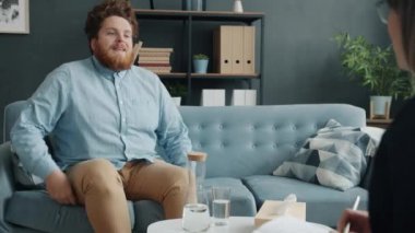 Terapiye gelen neşeli adam ofiste psikologla konuşuyor.