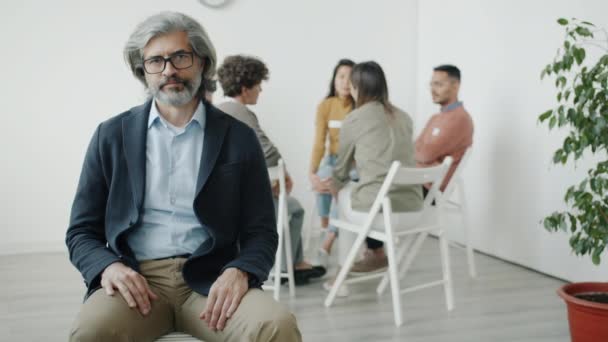Portrét depresivního dospělého muže při pohledu do kamery během skupinové terapie v interiéru — Stock video