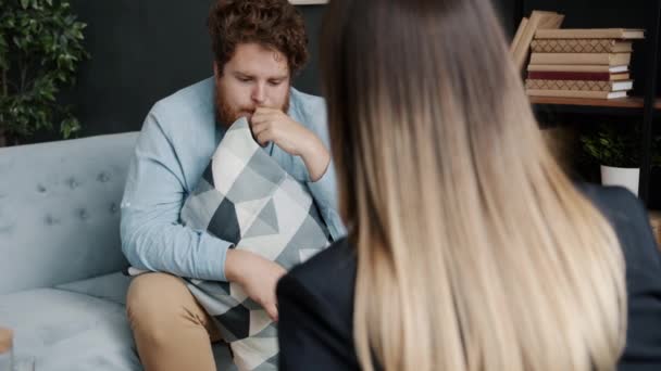 Uomo triste e nervoso che parla con lo psicologo condividendo sentimenti seduti sul divano abbracciando cuscino — Video Stock