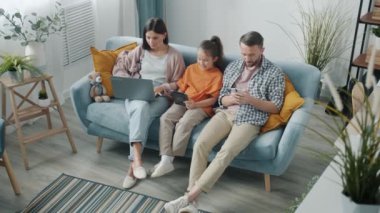 Mutlu aile aletleri kullanıyor ve konuşuyor modern apartmandaki koltukta dinleniyor.