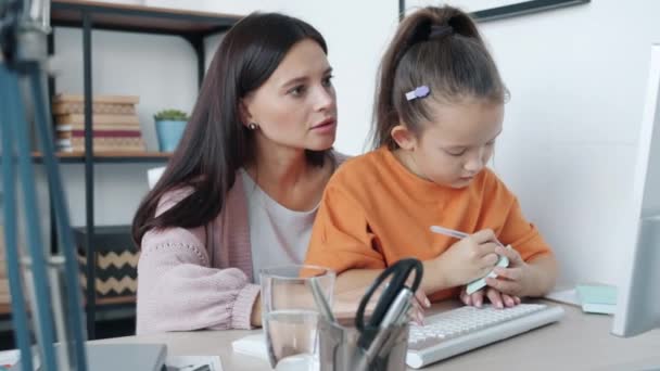 Cute little girl kissing mother while woman working with computer from home — Stock Video