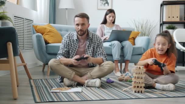 Apa és a kislány videojátékoznak, miközben anya laptoppal dolgozik. — Stock videók
