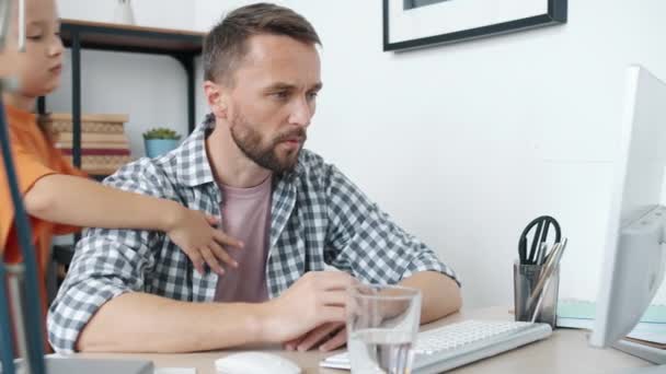 Evden bilgisayarla çalışan mutsuz babaya sarılan nazik küçük kız. — Stok video