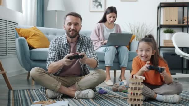 Mutlu aile video oyununun keyfini çıkarıyor. Çocuk evde yerde oturup oyuncaklarını kaybediyor ve kırıyor. — Stok video