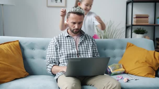 Ayah orang yang serius bekerja dengan laptop sementara putri mempercantik dia dengan bijouterie — Stok Video