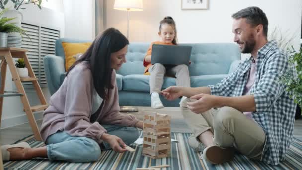 Padres alegres jugando con juguetes mientras niña seria trabajando con computadora en casa — Vídeos de Stock