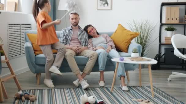 Parents fatigués mère et père assis sur le canapé regardant malheureux tandis que la fille active courir autour — Video