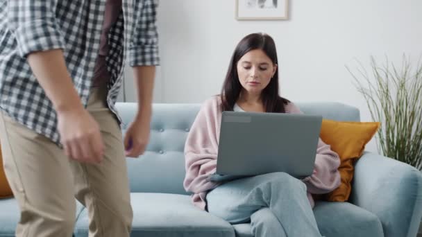 Втомився чоловік сидить на дивані, розмовляючи з дружиною, дивлячись на екран ноутбука — стокове відео