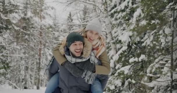 Slow motion porträtt av glad man ha kul med flickvän kör bär kvinna i skogen på vintern — Stockvideo
