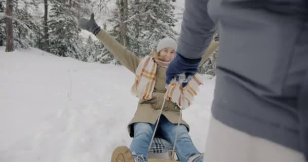 Портрет веселой леди, наслаждающейся поездкой, в то время как мужчина тянет сани в зимнем лесу — стоковое видео