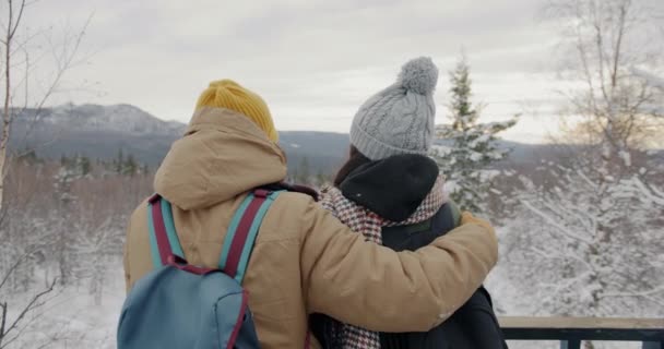 Мужчина и женщина зимой наблюдают за горами, наслаждаясь объятиями на открытом воздухе — стоковое видео