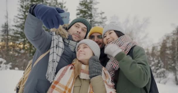 Разнообразная группа туристов делает селфи с камерой на смартфоне, позируя в зимнем лесу — стоковое видео