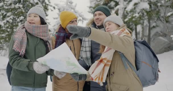 Wieloetniczna grupa turystów patrząca na mapę i rozmawiająca razem o wędrówkach po pięknym zimowym lesie — Wideo stockowe