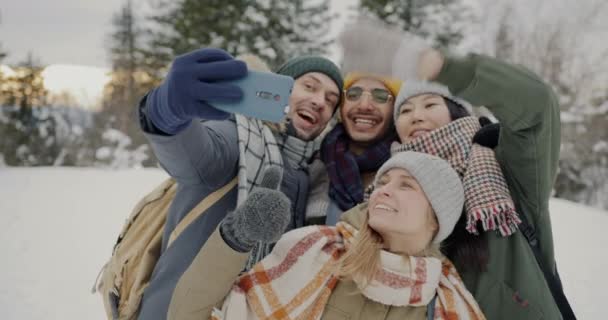 Joyful friends taking selfie with smartphone camera posing with thumbs-up gesture and laughing in winter forest — Stock Video