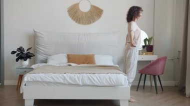 Pijama giyen neşeli bir kadının portresi. Yatağa düşüyor. Rahat bir yatak odasında dinleniyor.