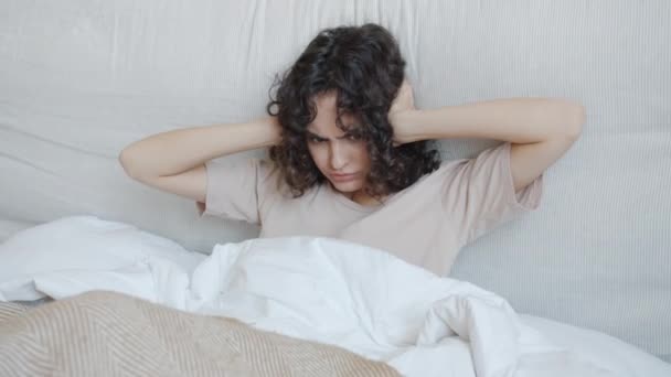 Unzufriedene junge Frau kann nicht schlafen, weil laute Geräusche Ohren mit Händen im Bett bedecken — Stockvideo