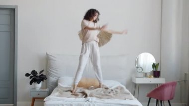 Pijamalı ve göz bantlı mutlu genç bir kadının portresi. Yatakta dans edip müzik dinliyor.