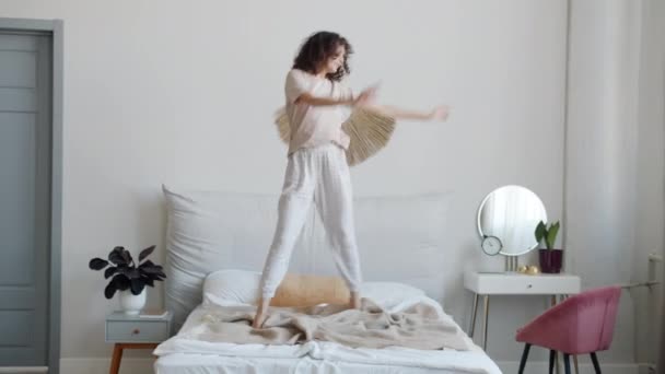 Porträtt av glad ung kvinna med pyjamas och ögonlappar dansar i sängen njuter av musik — Stockvideo