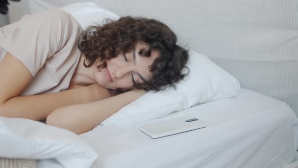 Junge Frau schläft im Bett, dann wacht sie auf und berührt Smartphone-Bildschirm — Stockvideo