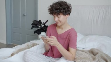 Yatakta akıllı telefon kullanarak pijama giyen güzel bir kızın yavaş çekim portresi.