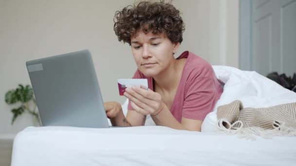 ベッドで幸せを表現クレジットカードで支払うラップトップでオンラインショッピング楽しい若い女性 — ストック動画