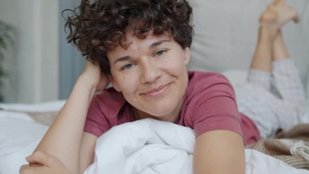 Retrato de chica encantadora con pijamas cómodos acostado en la cama en casa sonriendo — Vídeo de stock
