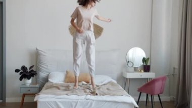 Pijamalı neşeli kız öğrenci yatakta zıplıyor ve evde eğleniyor.