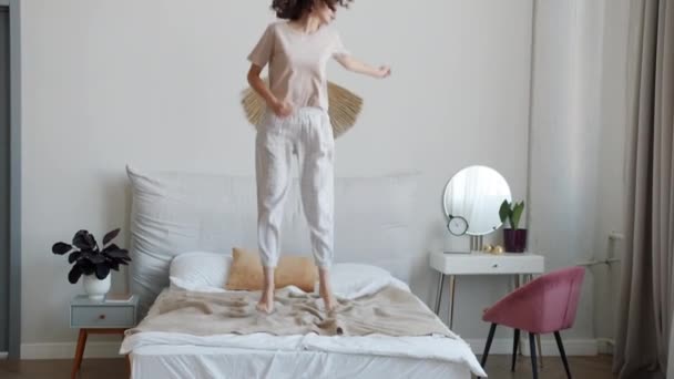 Χαρούμενη μαθήτρια που φοράει πιτζάμες πηδώντας στο κρεβάτι διασκεδάζοντας απολαμβάνοντας ελεύθερο χρόνο στο σπίτι — Αρχείο Βίντεο