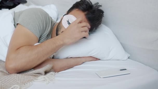 Hombre árabe con máscara de sueño despertando y usando teléfono inteligente en la cama en casa — Vídeo de stock