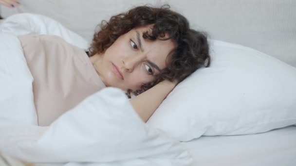 Mujer joven infeliz despertando y cubriendo oídos con almohadas odiando el ruido — Vídeo de stock