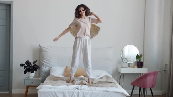 穿着舒适睡衣的年轻女子的慢动作肖像，在床上跳得很开心 — 图库视频影像