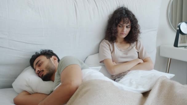 Арабський хлопець спить, коли божевільна жінка з Кавказу дивиться на нього, відчуваючи себе сердитим у ліжку. — стокове відео