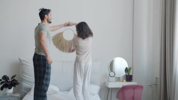 Feliz jovem casal árabe homem e mulher caucasiana dançando na cama desfrutando de manhã despreocupada em casa — Vídeo de Stock