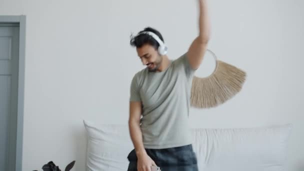 Loco hombre de Oriente Medio bailando en la cama escuchando música a través de auriculares — Vídeo de stock