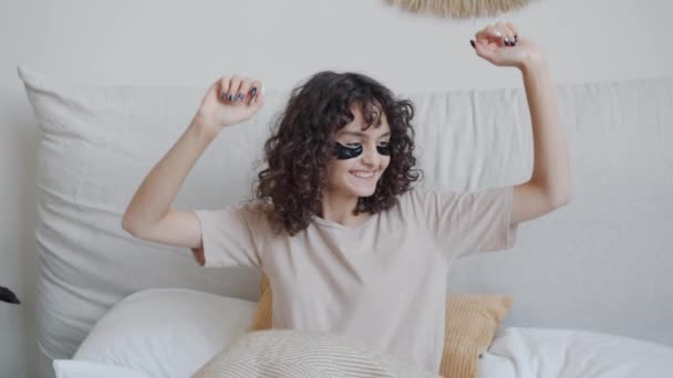 Retrato de joven alegre con parches para los ojos bailando en la cama relajándose el fin de semana — Vídeo de stock