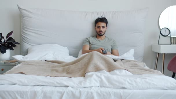 Glad arabisk kille tittar på TV och skrattar njuter av komedi show i sängen hemma — Stockvideo