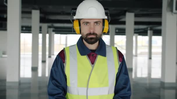 Retrato en cámara lenta del trabajador de la construcción que usa casco de seguridad y auriculares en interiores — Vídeo de stock