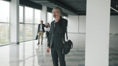 İş adamı cep telefonuyla konuşuyor sonra da bina içinde inşaatçıyla konuşuyor.