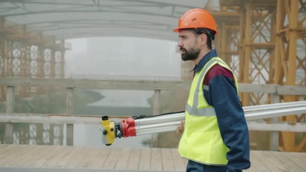 Zeitlupe des Vermessungsingenieurs in Uniform, der auf der Baustelle Theodolit hält — Stockvideo