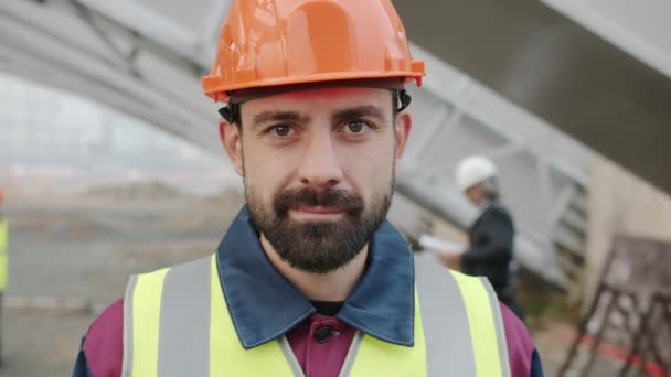 Portret van een jonge ingenieur die in de buitenlucht op het werk staat te glimlachen en naar de camera kijkt — Stockvideo