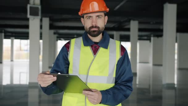 Retrato de especialista em construção em pé no local de trabalho com papéis e olhando para a câmera — Vídeo de Stock
