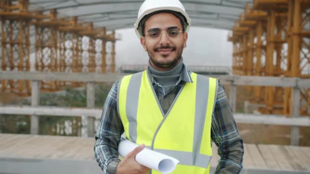 Retrato de un chico guapo de Oriente Medio con casco de seguridad y plan de construcción. — Vídeo de stock