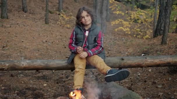 Slow motion portrait of joyful kid sitting near campfire holding roasted marshmallow smiling — Stock Video