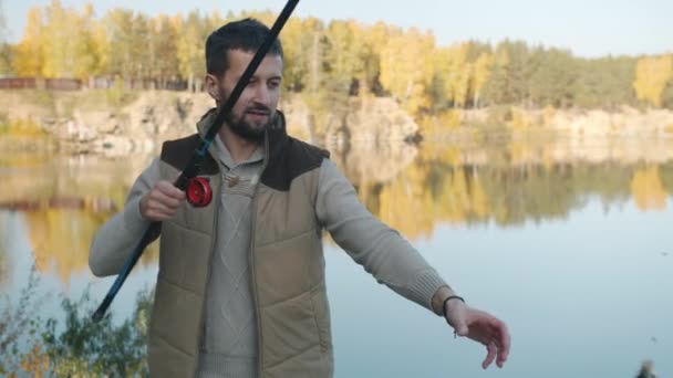 Porträtt av attraktiv skäggig kille fånga fisk och ler mot vacker bakgrund — Stockvideo