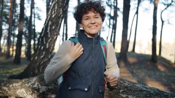 Porträt einer attraktiven Backpackerin, die mit glücklichem Lächeln im Wald steht — Stockvideo